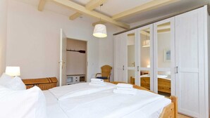 A bedroom with a large bed, a wardrobe, and a chair. - Remise Whg. 13 - Villa Bellevue (Heringsdorf)