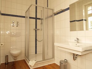 Kylpyhuone, jossa on lasiseinällä varustettu suihku, valkoinen pesuallas ja wc.