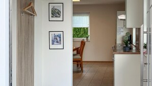 A modern kitchen with white cabinets, a dining area with a wooden table and chairs, and two framed pictures on the wall.