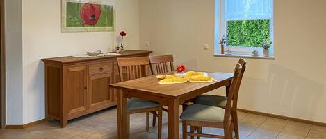A dining area with a wooden table and chairs, a wooden cabinet, and a window with a view of greenery.