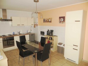 Een kleine keuken met een eettafel, stoelen, een kookplaat, een gootsteen en een koelkast.