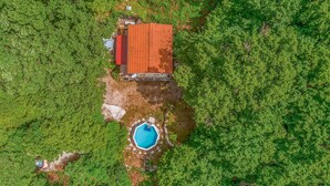 Vista aérea de una casa con techo rojo, rodeada de abundante follaje verde.