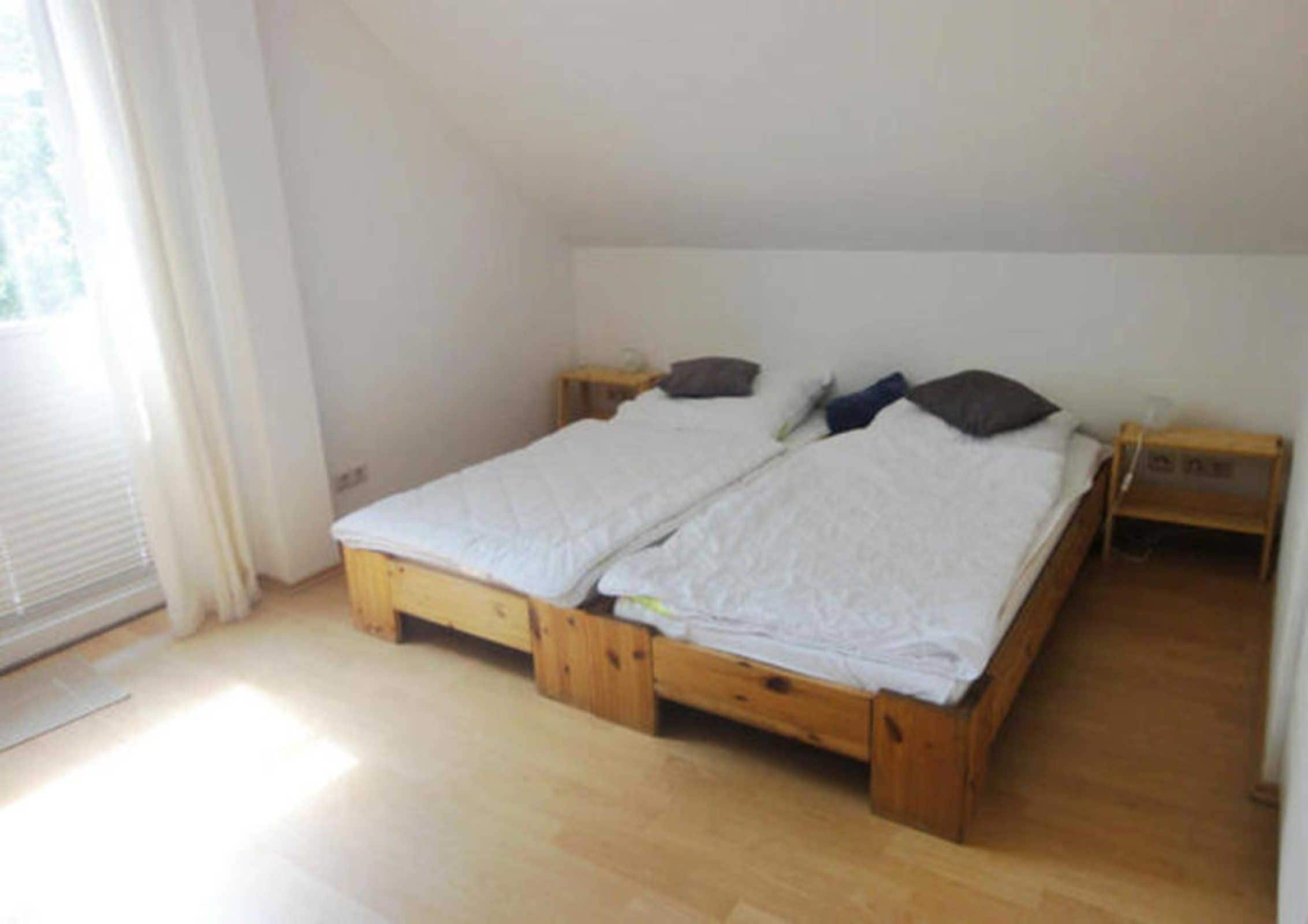 Una habitación con una cama de madera, una mesita de noche y una ventana con cortinas.