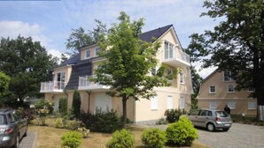 Een woonhuis met balkon, oprit en gazon met struiken.