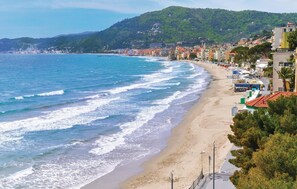 Uma cidade costeira com praia de areia, edifícios à beira-mar e um relevo montanhoso ao fundo.