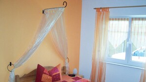 Un dormitorio con cama, mesita de noche, ventana con cortinas y lámpara de pared.