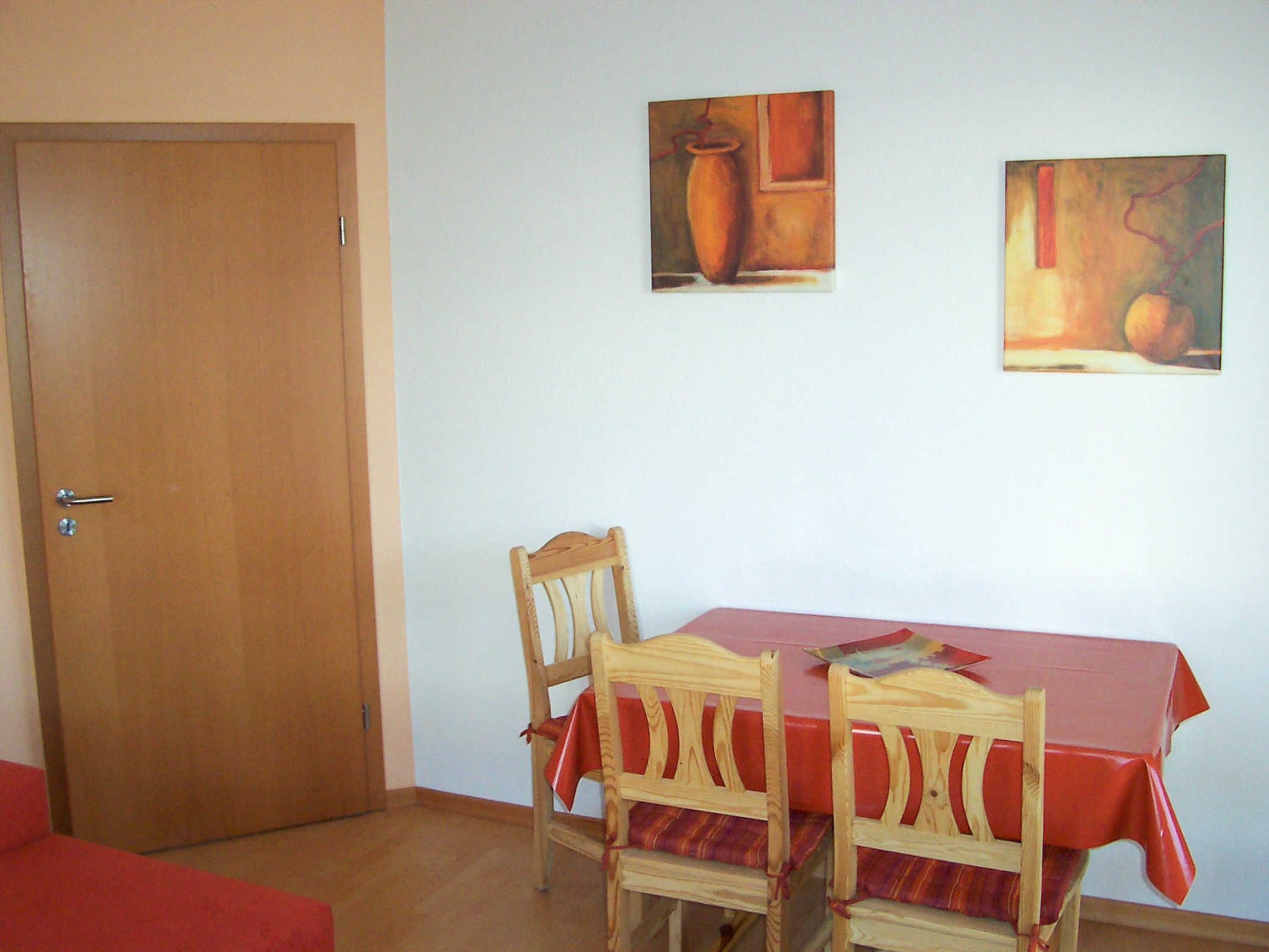 Un coin repas avec une table et des chaises en bois, une nappe rouge et deux tableaux accrochés au mur.