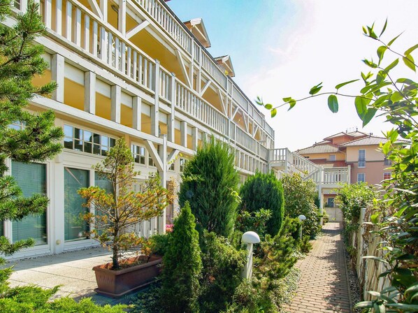 Un edificio de varios pisos con balcones, un camino de ladrillo y diversas plantas y arbustos.