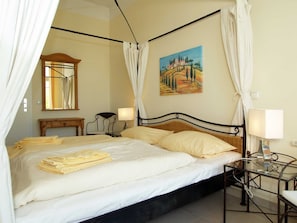 A bedroom with a bed, bedside lamps, a painting, and a mirror.