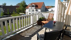 A balcony with a table and chairs, a white railing, and a view of a house with a red roof. - beach street 14-09 . - 14-09 (Kühlungsborn)