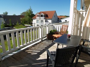 A balcony with a table and chairs, a white railing, and a view of a house with a red roof.
