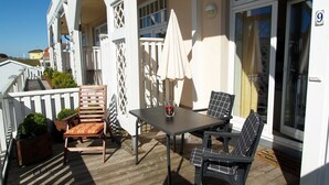A covered outdoor seating area with a table and chairs, a white fence, and a building with a number '9' sign. - beach street 14-09 . - 14-09 (Kühlungsborn)