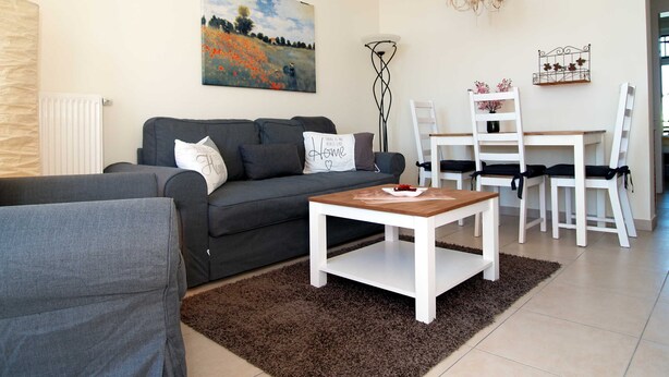 A modern living room with a grey sofa, a coffee table, a dining table with chairs, a chandelier, and a painting on the wall. - beach street 14-09 . - 14-09 (Kühlungsborn)