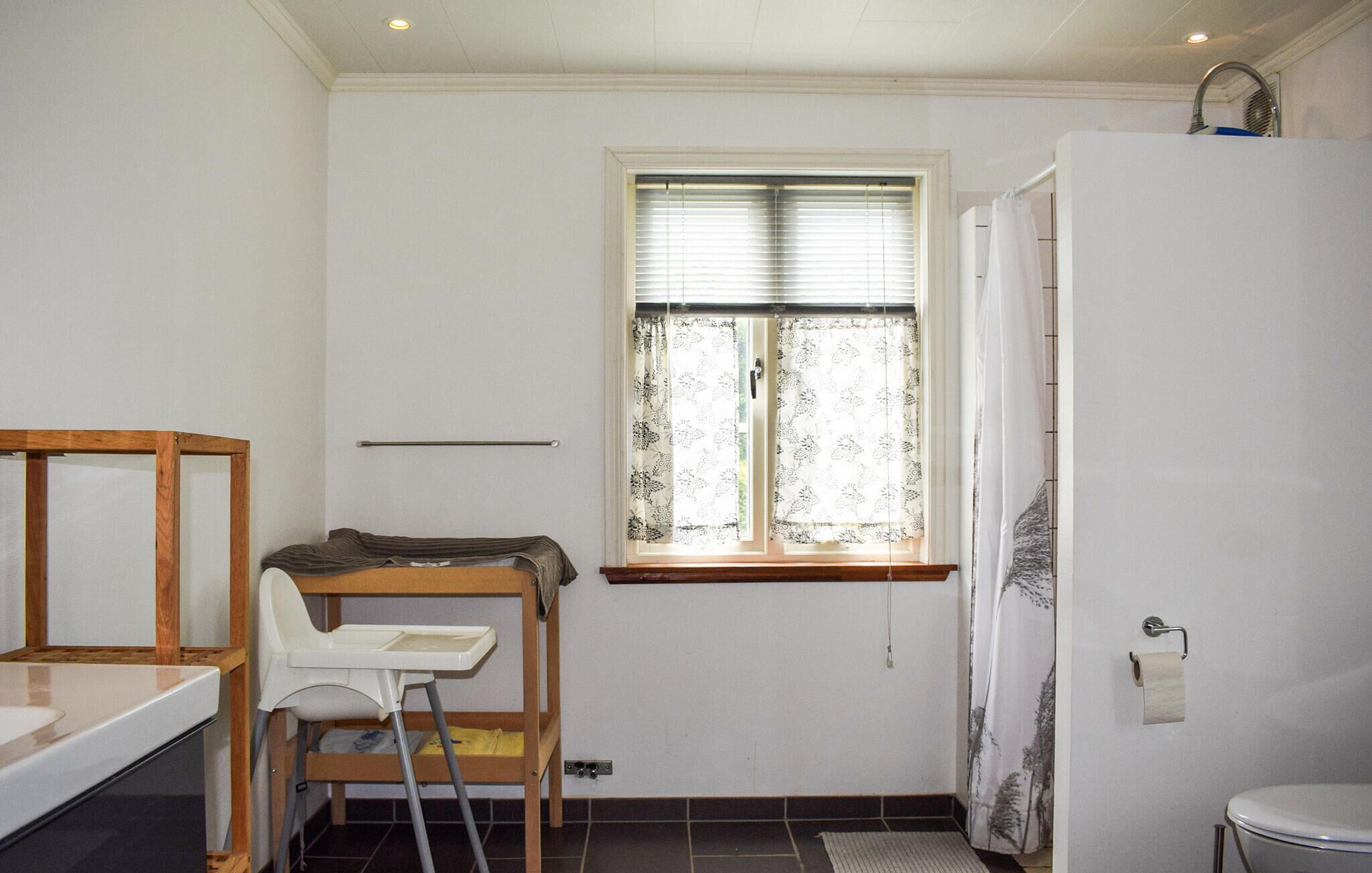 Una habitación pequeña y funcional con ventana, ducha, lavamanos y una silla.