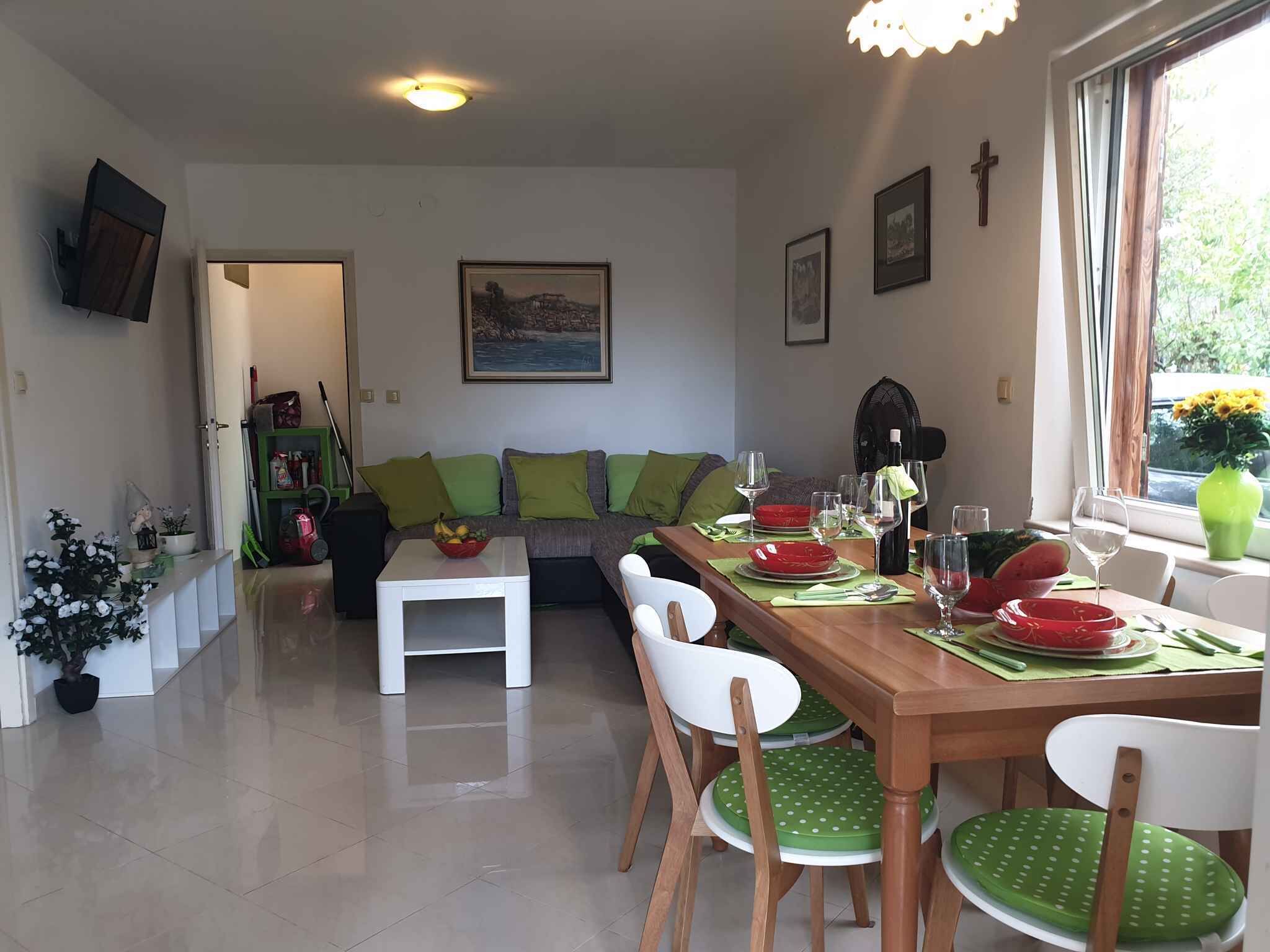 Un comedor con una mesa de madera dispuesta para cuatro personas, sillas verdes y un sofá blanco con cojines verdes.
