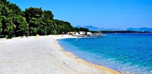 En strand med klart, blåt vand, sand og en båd i baggrunden.