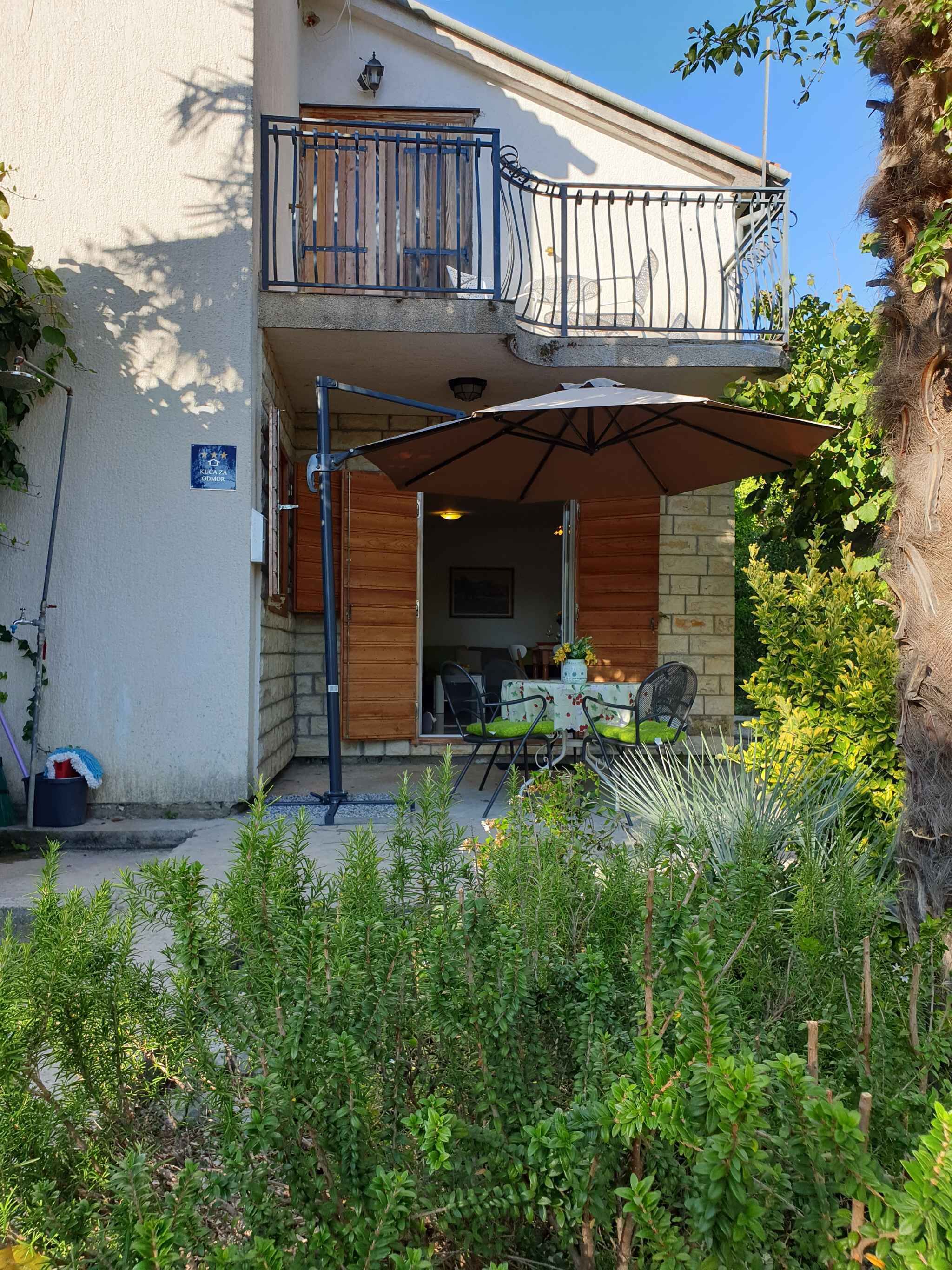 Un edificio de dos pisos con balcón, zona de estar al aire libre y un letrero que indica un espacio público.
