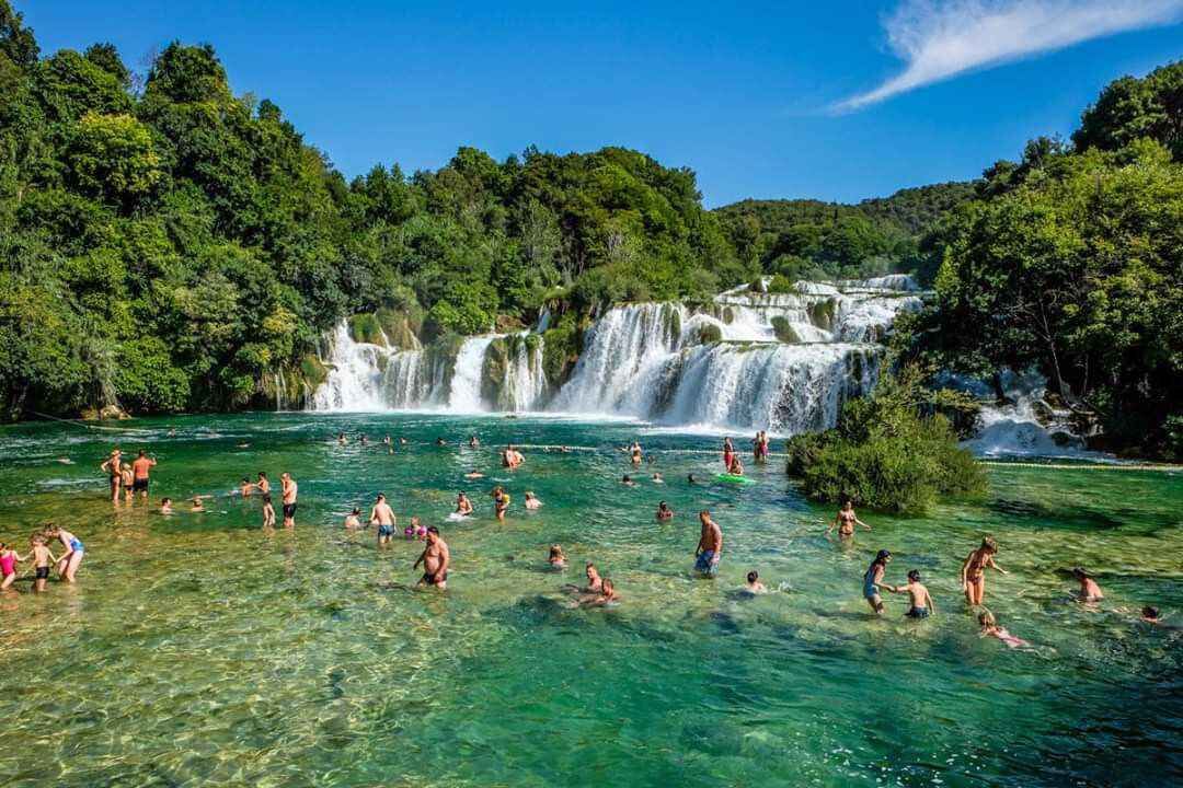 Entorno natural con cascada y agua cristalina, rodeado de abundante vegetación.