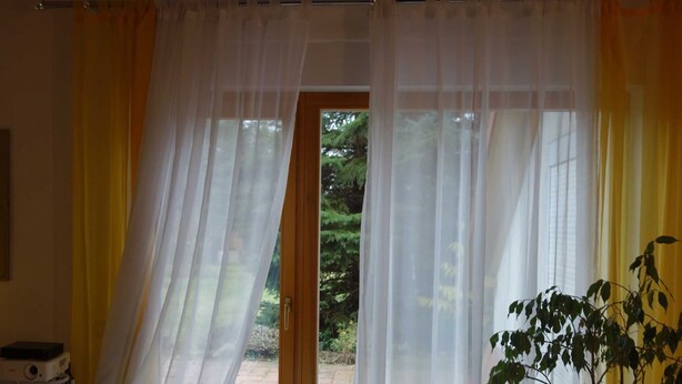 A bedroom with a bed, a projector, and a view of a garden through sheer curtains. - Moni's Surfhaus - double room 1 (Rechlin)