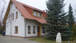 A two-story house with a red-tiled roof, a front porch, and a large evergreen tree in front. - Moni's Surfhaus - double room 1 (Rechlin)