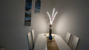 A dining area with a round table, four chairs, a vase with flowers, and a decorative light fixture. - Moni's Surfhaus - double room 1 (Rechlin)