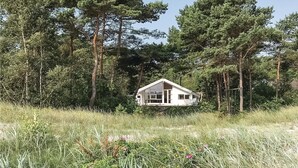 A small, white cabin surrounded by tall trees and dense grass. - Stunning home in Nexø with kitchen (Nexø)