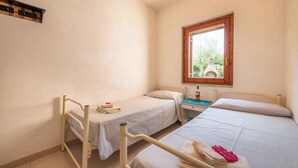 Une petite chambre propre, avec deux lits simples, une fenêtre donnant sur un paysage verdoyant et une tête de lit en bois.