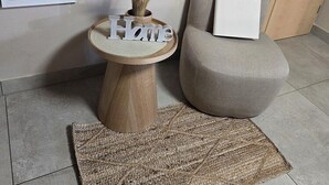 A modern living room with a round wooden side table, a grey armchair, and a mirror reflecting a sofa. - Gästehaus Alwin Diebold (Rust)