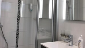 A modern bathroom with a glass-enclosed shower, a white sink with a dark cabinet, and a mirror above the sink. - Gästehaus Alwin Diebold (Rust)