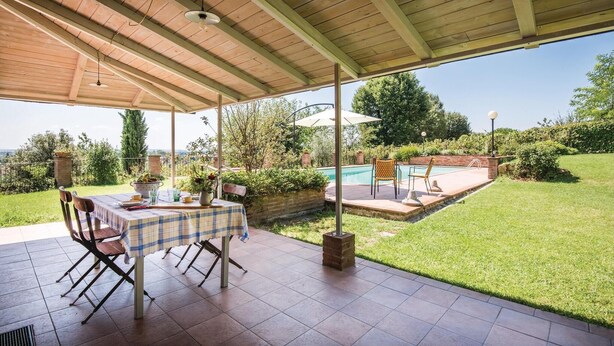 Un patio al aire libre con mesa y sillas, una piscina y una zona ajardinada.