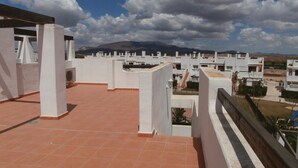 Una terraza en la azotea con paredes blancas y tejas de terracota, con vistas a una zona residencial y montañas al fondo.