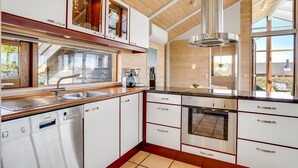 A modern kitchen with a dishwasher, oven, and a large window overlooking a garden. - 2 bedroom stunning home in Sjølund (Sjølund)