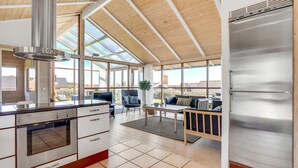 A modern kitchen with a stainless steel refrigerator, a built-in oven, and a large windowed dining area. - 2 bedroom stunning home in Sjølund (Sjølund)