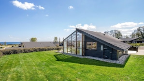 A modern house with a large glass window, a sloped roof, and a well-maintained lawn. - 2 bedroom stunning home in Sjølund (Sjølund)