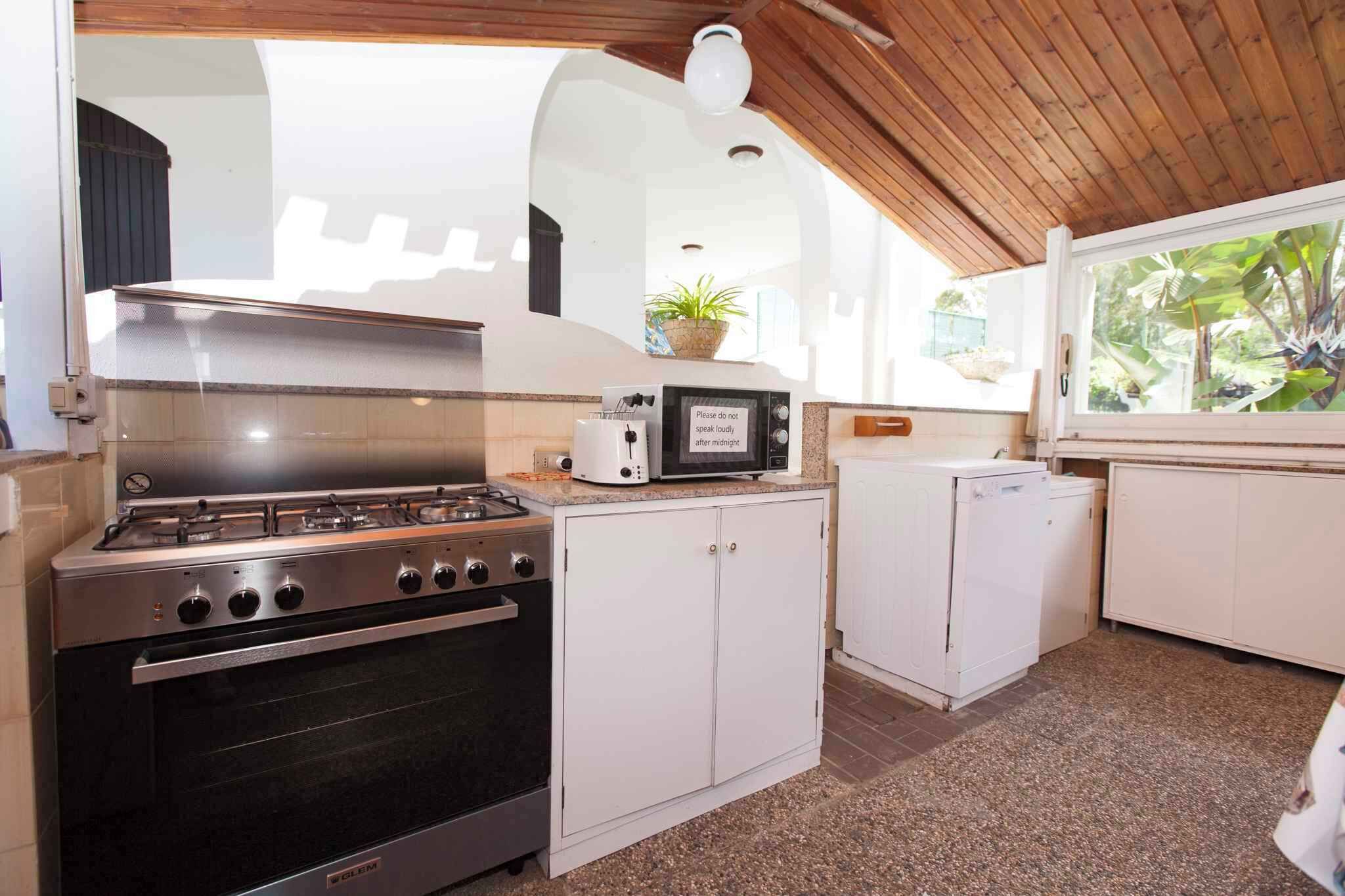 Une cuisine de taille réduite, équipée d’une cuisinière à gaz, d’un four à micro-ondes et de meubles de rangement blancs.