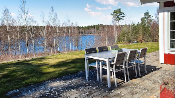 Un espace extérieur aménagé pour les repas, avec une table et des chaises, une pelouse verdoyante et une vue sur un lac et des arbres.