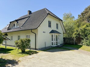 Une maison à deux étages, avec un toit en tuiles, un porche à l’avant et un petit jardin.