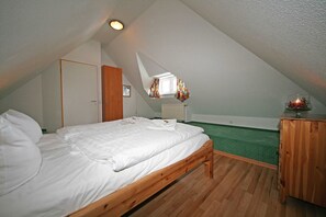 Une chambre avec un plafond en pente, un lit en bois, une petite fenêtre avec des rideaux, un radiateur et une moquette verte.