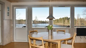 A dining area with a round table and four chairs, a pendant light, and a view of a lake through large windows.