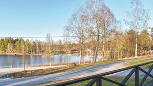 A lakeside road with a wooden bridge railing, a calm lake, and trees in the background.