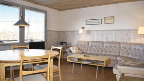 A cozy living room with a wooden ceiling, a round dining table with chairs, a cushioned sofa, and a coffee table.
