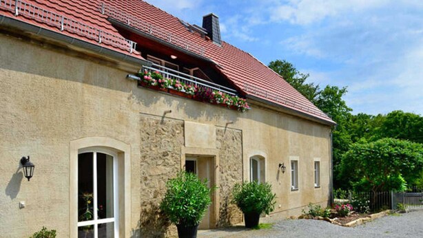 A stone building with a red-tiled roof, a balcony with flowers, and potted plants in front. - Apartment 2 - 32sqm (2 persons), balcony - Weichaer Hof FBS Sonja Fritsch & (Weißenberg)