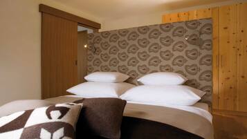 A bedroom with a bed, pillows, a blanket, wooden walls, and a patterned wallpaper.