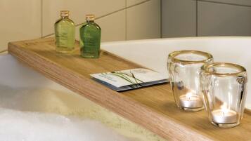 A wooden tray with two bottles of Pure Herbs bath products and two glass candle holders with candles on a bathroom counter.