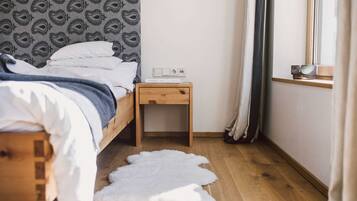 A bedroom with a wooden bed, a bedside table with a power outlet, a white rug, and a window with curtains.