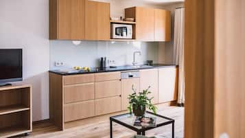 A modern kitchen with wooden cabinets, a microwave, and a sink. There is a glass coffee table with a magazine and a plant.