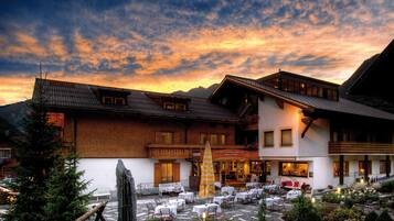 A hotel with outdoor seating, a stone facade, and a mountain backdrop.