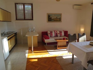 A compact kitchen with a dining area, a sofa, and a painting on the wall.