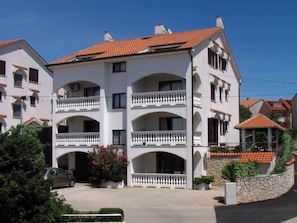 A multi-story building with balconies, a stone wall, and a car parked in front.