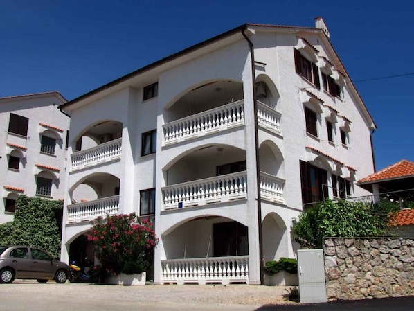 A multi-story building with balconies, a stone wall, and a parked car.